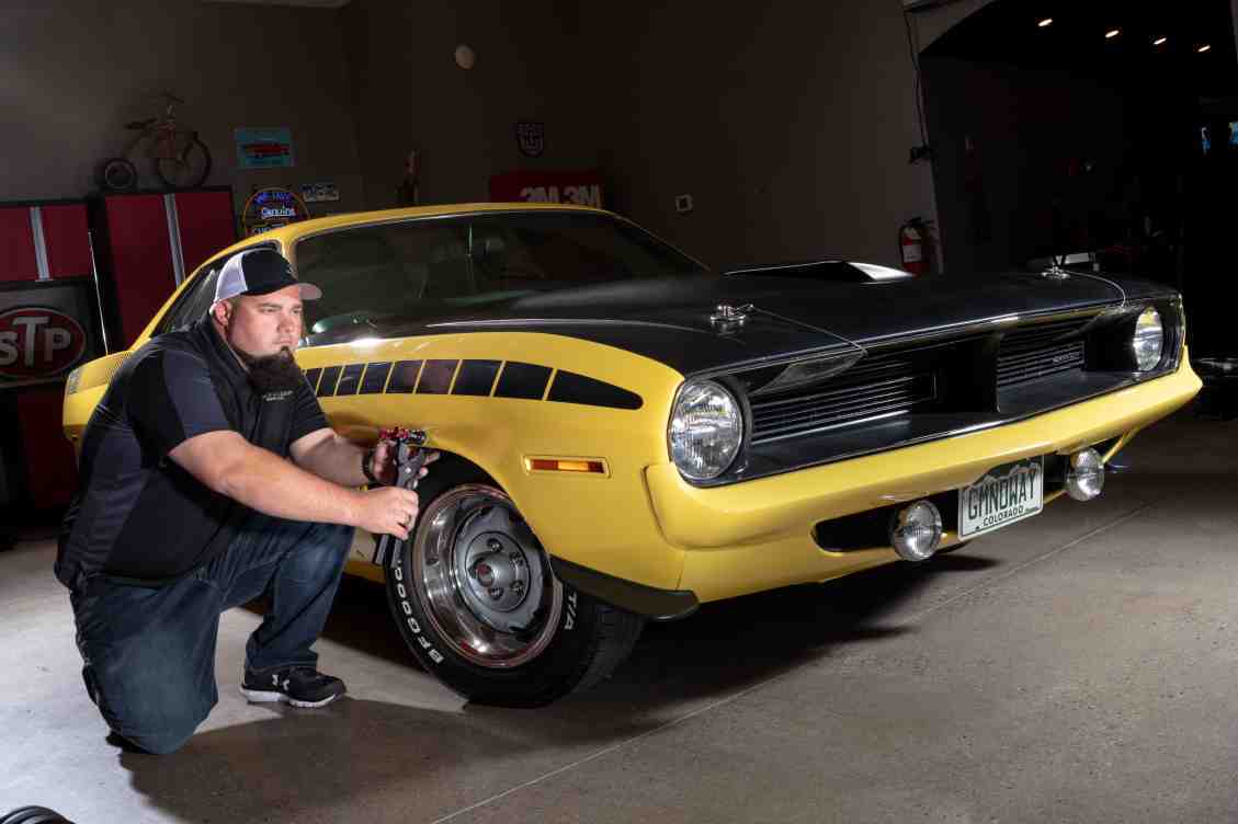 A man kneeling next to a yellow muscle car.